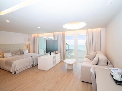 Jasny pokój hotelowy z podwójnym łóżkiem, sofą, telewizorem z płaskim ekranem i balkonem z widokiem na morze.