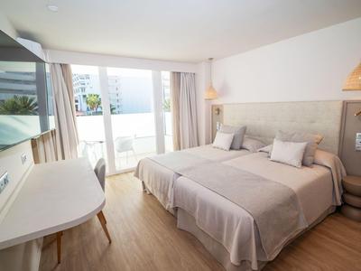 Hell eingerichtetes Hotelzimmer mit zwei Einzelbetten und Balkon mit Blick auf das Meer.