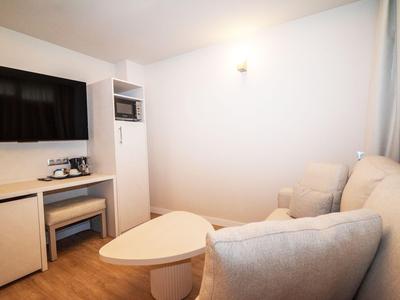 Kleine Hotelzimmer-Lounge mit grauem Sofa, rundem Tisch und Fernseher an der Wand.