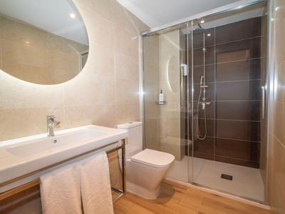 Modernes Hotelbadezimmer mit großer Waschfläche, Toilette und Glasdusche mit dunklen Fliesen.