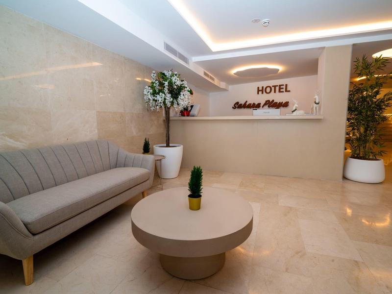 Elegante vestíbulo de hotel con mesa redonda, sofá y plantas en un ambiente moderno.