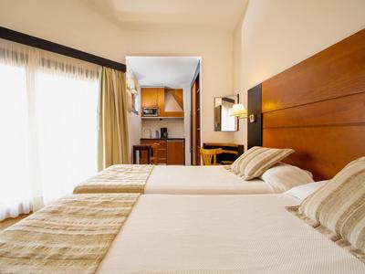 Lichte hotelkamer met twee eenpersoonsbedden, houten hoofdeinde en gordijnen bij het raam.