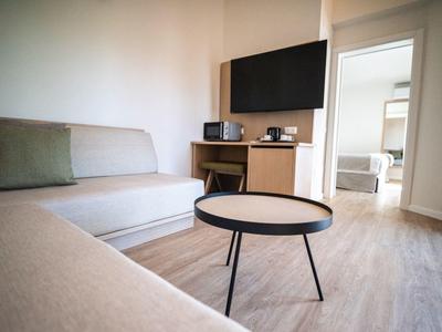 Modern woonkamer met bank, salontafel, tv en uitzicht op aangrenzende slaapkamer.