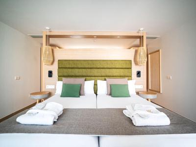 Moderne hotelkamer met groot bed, groen hoofdeinde en badjassen op het deken.