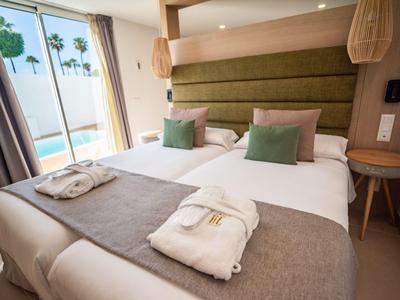 Modernes Hotelzimmer mit Doppelbett, Meerblick durch Glasfenster und Bademänteln auf der Bettdecke.