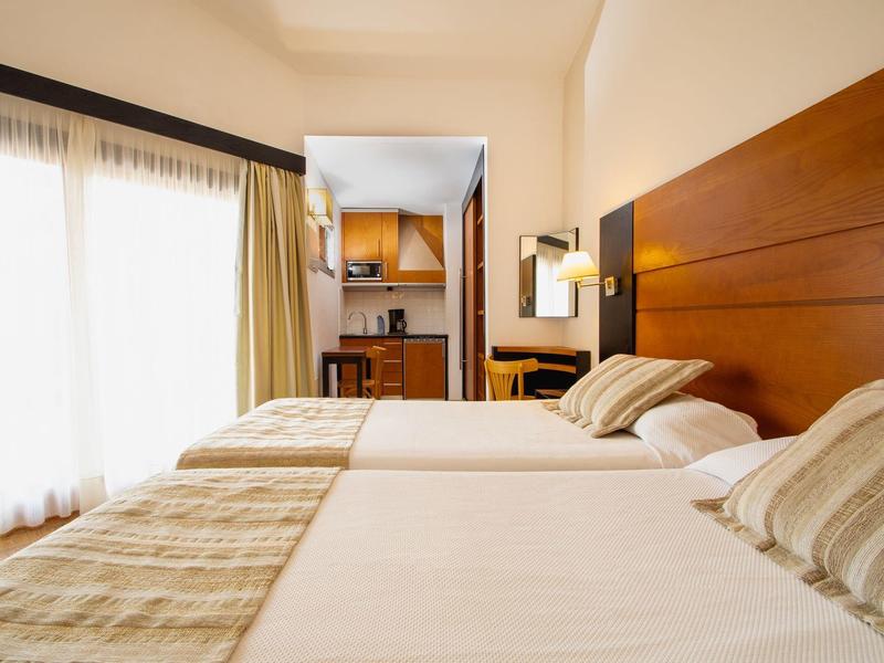 Lichte hotelkamer met twee eenpersoonsbedden, houten hoofdeinde en gordijnen bij het raam.