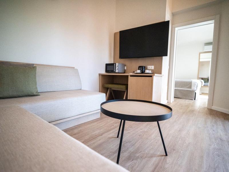 Modern woonkamer met bank, salontafel, tv en uitzicht op aangrenzende slaapkamer.