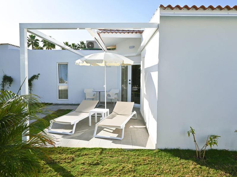 Moderne witte tuin met ligstoelen, parasol en gazon.