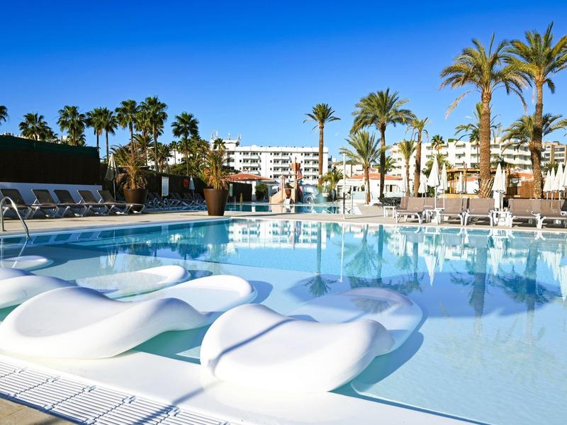 Moderne hotelzwembad met witte waterligstoelen en palmbomen onder blauwe lucht