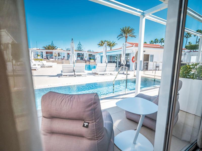 Uitzicht op een zwembad met witte ligstoelen en palmbomen vanaf een balkon.