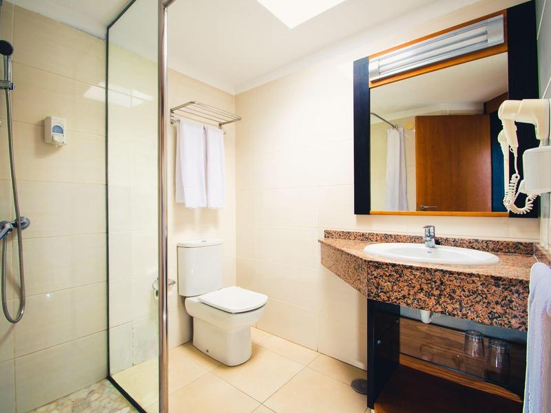 Lichte hotelbadkamer met douche, toilet, wastafel en grote spiegel.