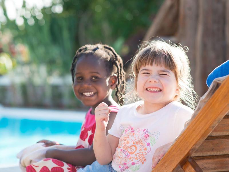 Twee lachende kinderen ontspannen op ligstoelen bij een zwembad.