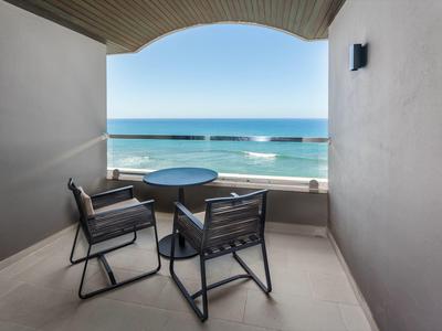 Balkon mit zwei schwarzen Stühlen, rundem Tisch und Blick auf das blaue Meer und den klaren Himmel.