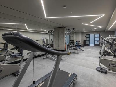 Moderner Fitnessraum mit Laufbändern, Fahrrädern, Spiegelwand und indirekter Deckenbeleuchtung.