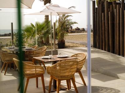 Gemütliche Terrasse mit Rattanstühlen, Tisch, Sonnenschirmen und Palmen bei sonnigem Wetter.