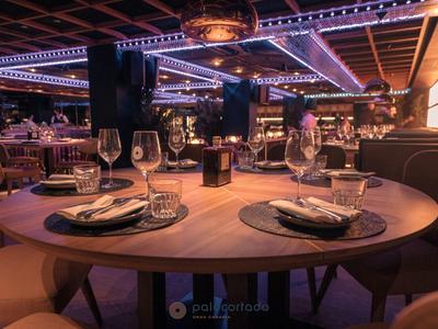 Elegantes Restaurant mit rundem Holztisch, gedeckten Plätzen und stimmungsvoller Lichtdecke.