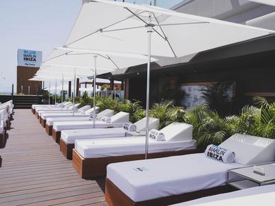 Reihe von weißen Liegestühlen mit Sonnenschirmen auf einer Hotelterrasse neben einer begrünte Wand.