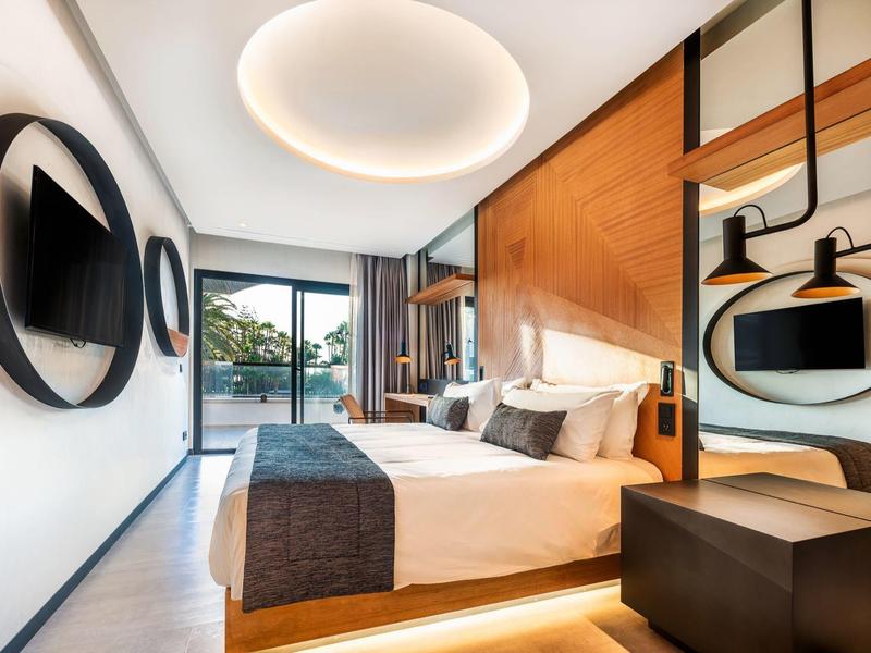 Habitación de hotel moderna con cama grande, espejos redondos y vistas a la naturaleza por ventanas grandes.