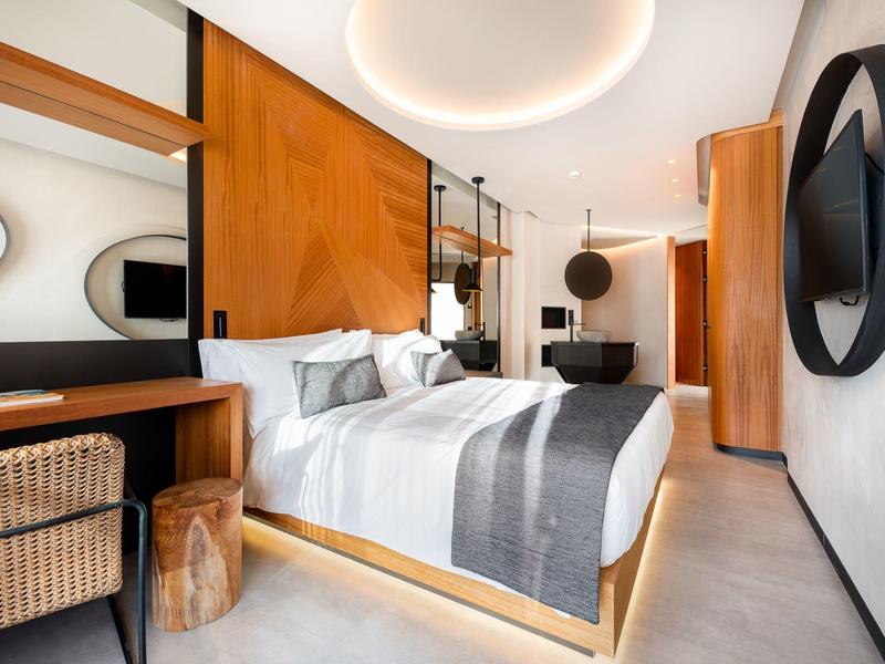 Habitación de hotel moderna con cama doble, detalles de madera y iluminación elegante.