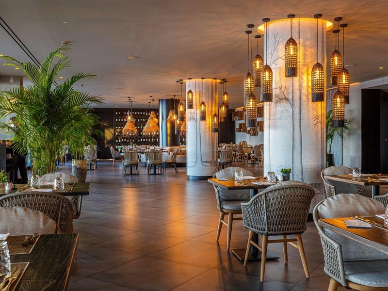 Elegante restaurante de hotel con luces modernas, decoración de mesas y áreas para sentarse junto a grandes ventanas.