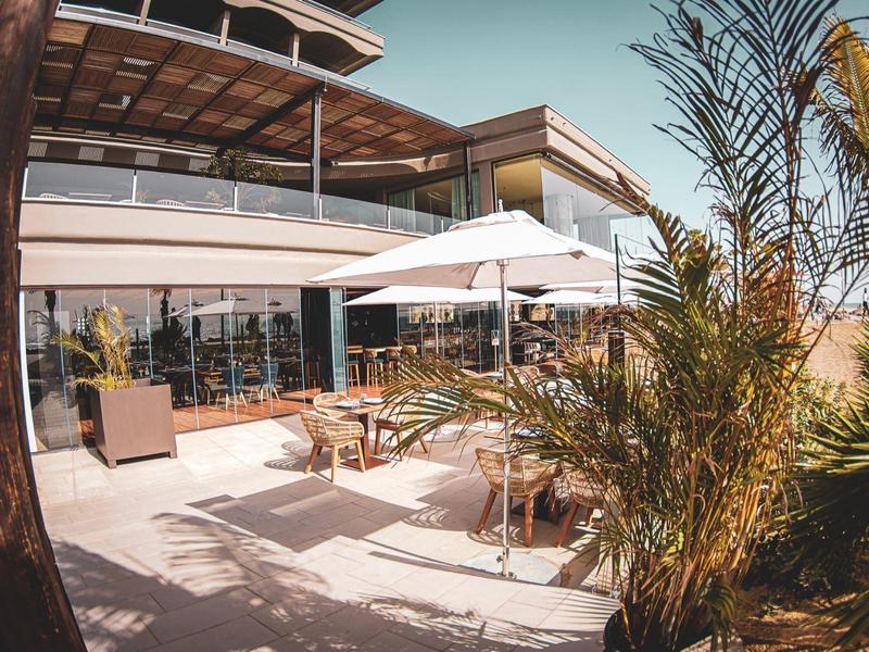 Terraza soleada de un hotel moderno con asientos y sombrilla bajo cielo azul.
