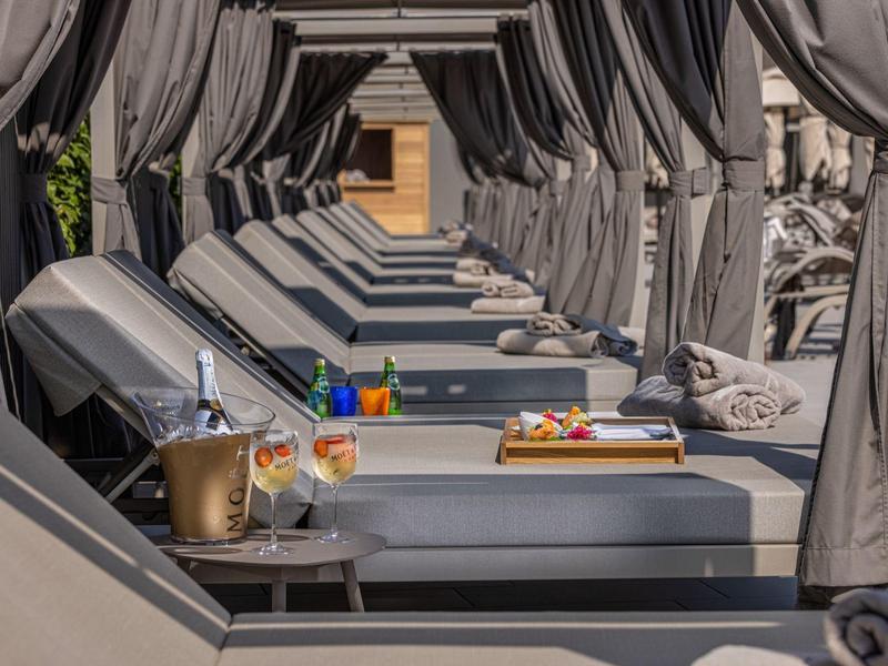 Lujosas camas con cortinas junto a la piscina con bebidas y aperitivos listos para relajarse.