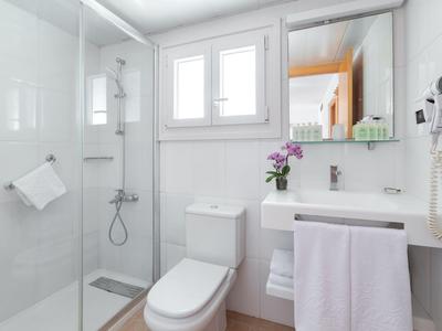 Bagno dell'hotel luminoso con sanitari bianchi, doccia, WC e lavabo.