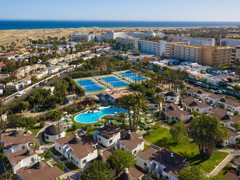 Aerial view of a coastal resort with white bungalows, swimming pools, and large hotels near the beach.