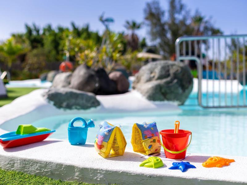 Colorful beach toys arranged near a swimming pool with rocks and green plants in the background.