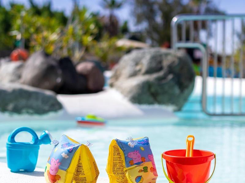 Colorful beach toys on pool edge with clear blue water and greenery in background