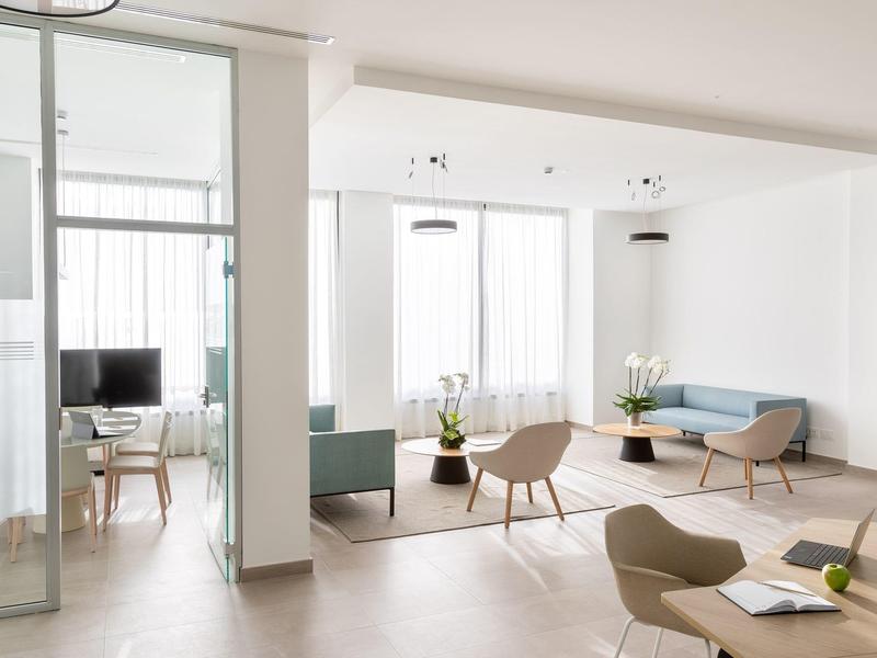 Sala de estar moderna y luminosa con asientos, mesas y grandes ventanas en un hotel.