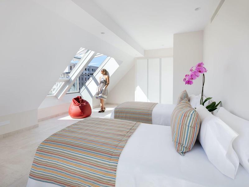 Dormitorio luminoso con dos camas, grandes ventanas y decoración moderna en una habitación de hotel.