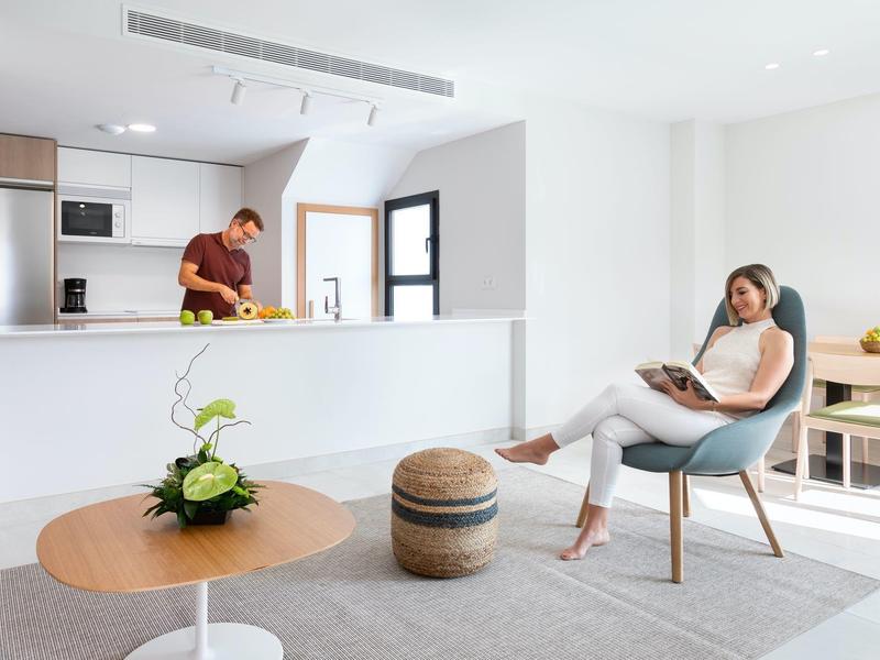 Apartamento moderno y luminoso con cocina abierta, hombre y mujer relajándose en sala elegante.