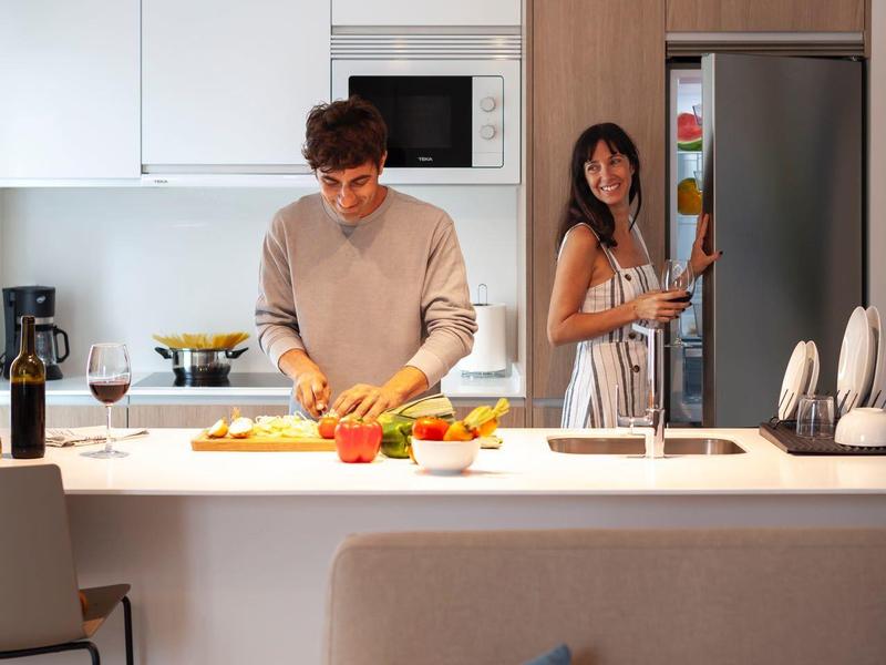 Cocina moderna con pareja preparando comida y frigorífico de acero inoxidable.