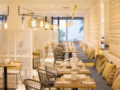 Modernes, helles Restaurant mit Tischen, Stühlen und dekorativen Kissen in einem Hotel.