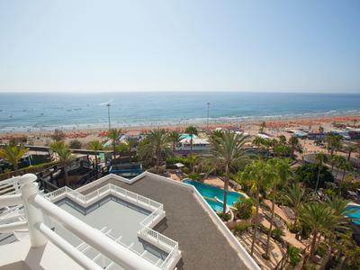 Blick auf Strand, Meer und Palmen von einer Hotelterrasse mit Pool im Vordergrund.