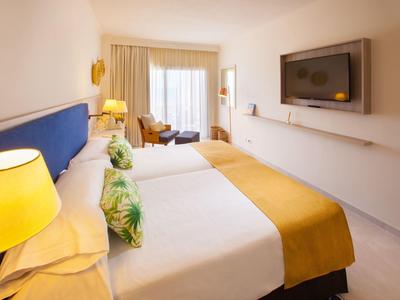 Hell eingerichtetes Hotelzimmer mit zwei Betten, gelben Decken und einem Fernseher an der Wand.