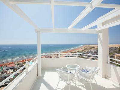 Balkon mit weißen Stühlen und Tisch mit Blick aufs Meer und den Strand.