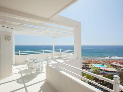 Terrasse mit weißem Geländer und Blick aufs blaue Meer und den Strand.