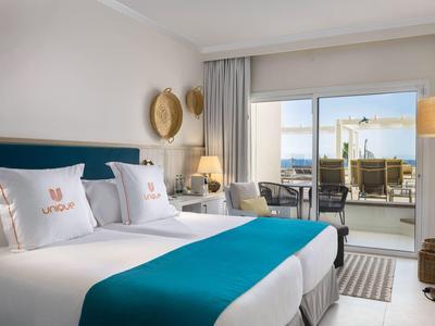 Modern eingerichtetes Hotelzimmer mit zwei Einzelbetten und Balkon mit Meerblick.