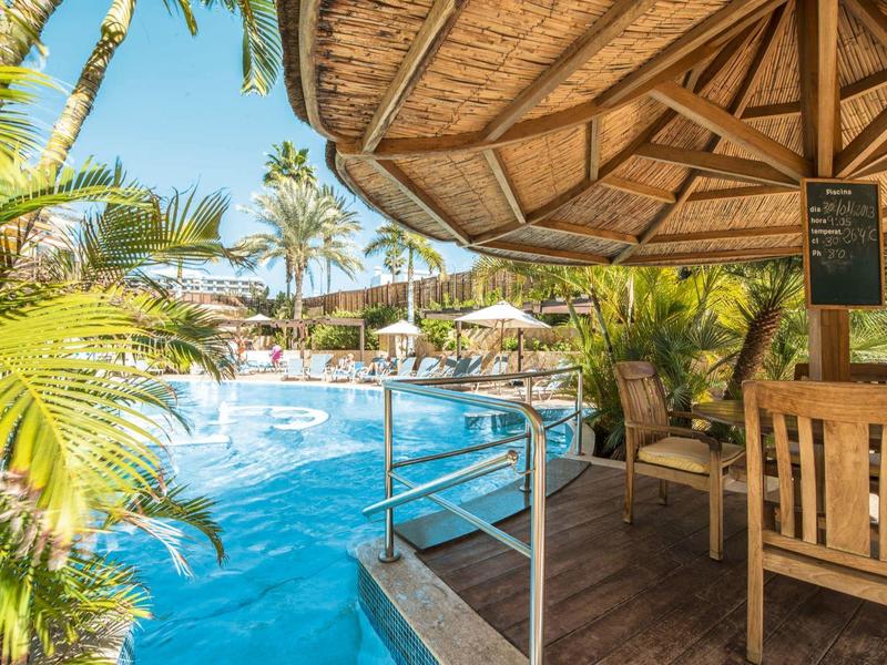 Poolbereich mit Stühlen, Sonnenschirmen und tropischen Pflanzen in einem Resort.