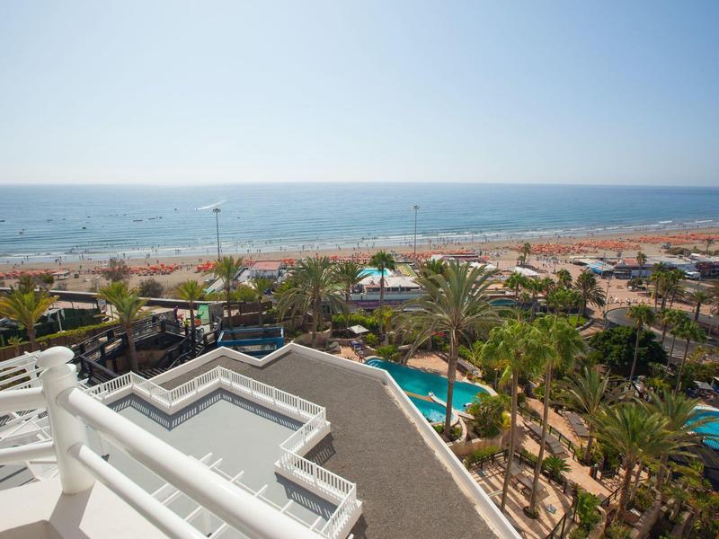 Blick auf Strand, Meer und Palmen von einer Hotelterrasse mit Pool im Vordergrund.
