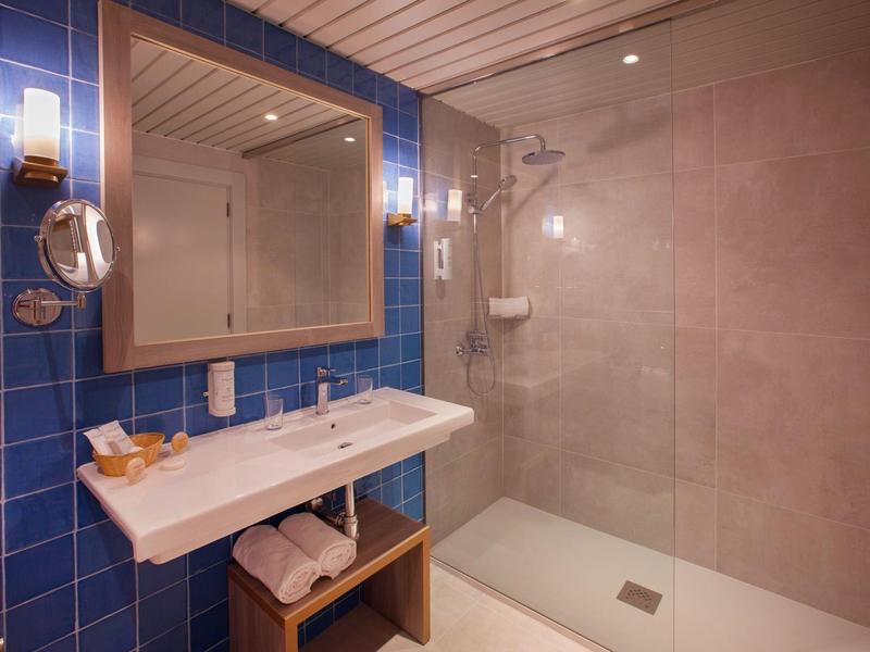Modernes Badezimmer mit blau gekachelter Wand, großem Spiegel, Waschbecken und begehbarer Dusche.