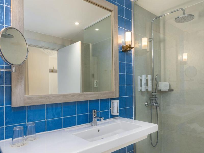 Modernes Badezimmer mit blauen Fliesen, großem Spiegel, Waschbecken und Dusche mit Glastür.