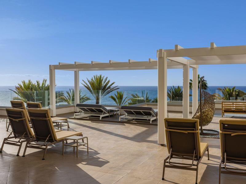 Terrasse mit Liegestühlen und Meerblick unter klarem blauem Himmel.