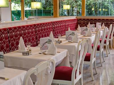 Elegant restaurant met witte tafelkleden, rode stoelkussens en grote ramen.