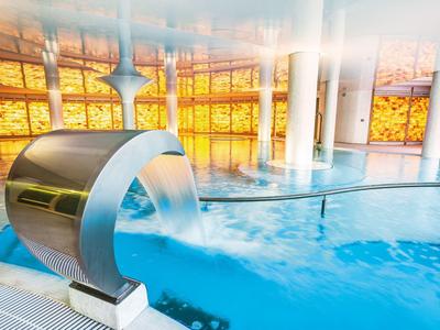 Modern indoor pool with waterfall feature and large glass windows with yellow lighting