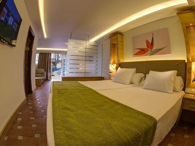 Modern hotelkamer met een tweepersoonsbed, groene deken en moderne verlichting.