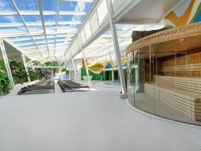 Modern spa area with glass walls, loungers, and a sauna in a bright, open space.