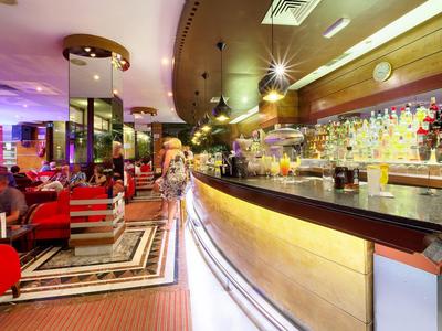 Modern hotel bar with stylish lighting, red armchairs, and well-stocked shelves behind the counter.